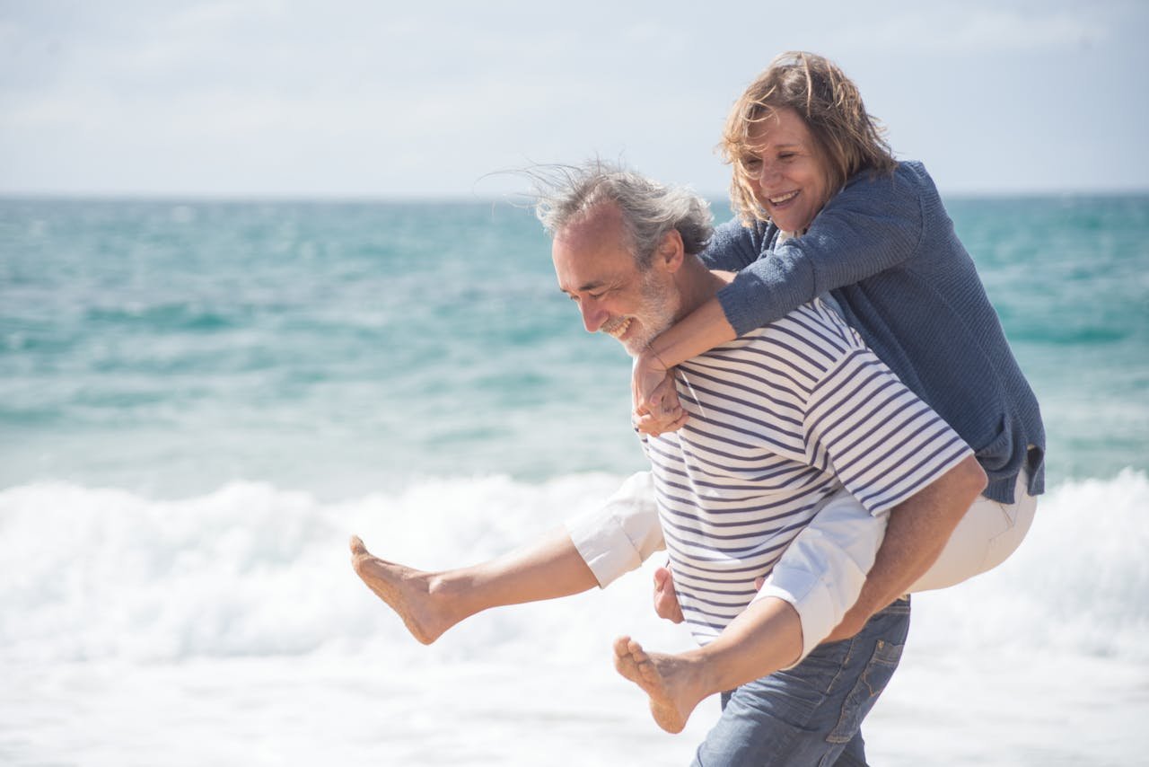 Happy senior couple on a beach in Portugal, sharing a joyful moment by the ocean.