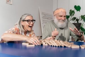 Elderly couple laughing and bonding while playing Jenga indoors.