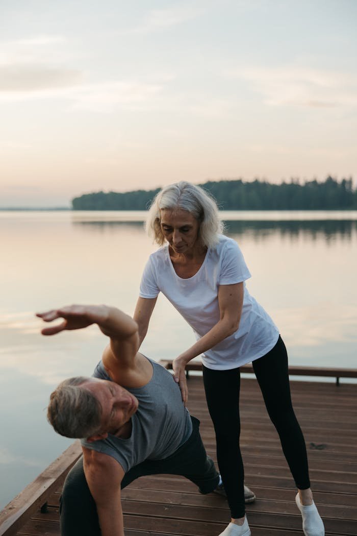 Senior couple practicing yoga on a tranquil lakeside wooden dock at sunrise.